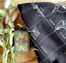 Load image into Gallery viewer, Terra Lenormand deck face down stack of cards between dried flowers and folded grand tableau cloth on a wood background