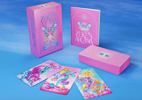 Zeke's Arcana box standing on end next to the guide booklet and the stacked card deck facedown. Three cards are facing up in front of the box. Everything is on a blue sky-like background